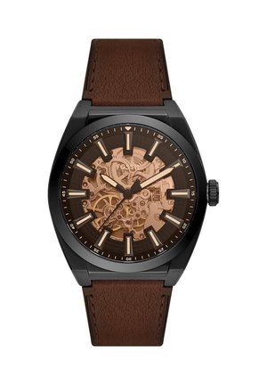Montre pour homme avec boîtier noir, bracelet en cuir marron, engrenages mécaniques en bronze exposés, et index et aiguilles lumineux.