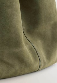 Olivengrøn suedetaske med glat tekstur, buet form og en synlig sømdetalje. Blødt, smidigt materiale uden hardware.