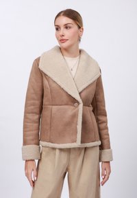 Brun kunstskinnjakke med en kremfarget shearling-krage og mansjetter, som har en enkelt knappelukking og en skreddersydd passform.