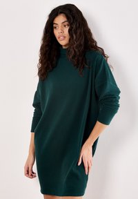 Rippenshwarzes, oversized Kleid mit hohem Ausschnitt und langen Ärmeln; der Stoff ist weich und leicht dehnbar.