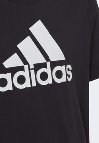 T-shirt nera in cotone con un grande logo Adidas bianco. Maniche corte, collo rotondo, texture liscia. Design semplice e moderno senza ulteriori motivi.