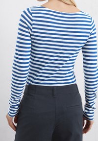 Niebiesko-biały, w paski, długi rękaw, wykonany z miękkiego materiału, z szerokim dekoltem i dopasowanym krojem, zestawiony z ciemnymi, dopasowanymi spodniami.