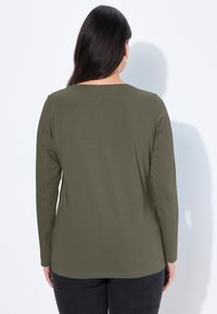 Olivenfarbene, langärmlige Bluse mit Rundhalsausschnitt, glatter Textur und lockerer Passform, kombiniert mit dunklen Hosen.