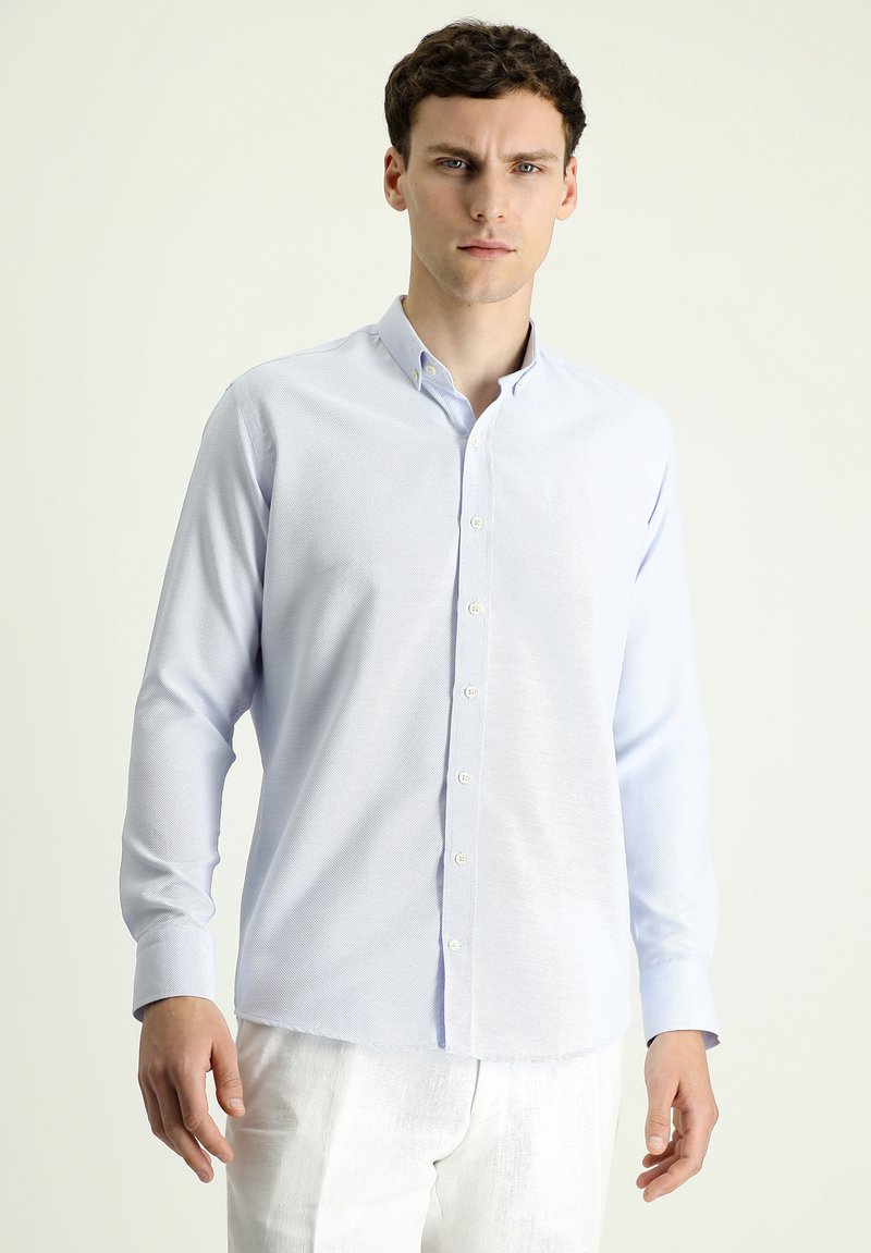 Camicia a bottoni azzurro chiaro con tessuto texturizzato, maniche lunghe e colletto classico; presenta bottoni bianchi lungo la parte anteriore.