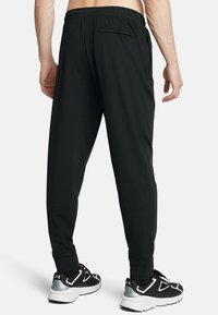 Zwarte atletische broek met een elastische tailleband en een achterzak met ritssluiting, voorzien van een tapered leg ontwerp en een zachte stofstructuur.
