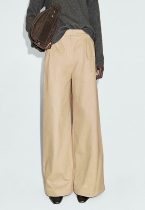 Pantaloni beige a gamba larga realizzati in tessuto leggero con una texture liscia e fronte plissettato, abbinati a una borsa in suede marrone.