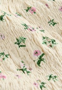 Tissu crème avec une apparence texturée et froissée, orné de délicieuses broderies florales en rose et vert tout au long.