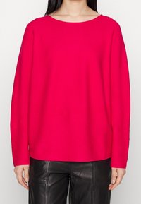 Pull en maille ample de couleur rose vif avec un large décolleté et des manches longues, associé à un pantalon en cuir noir taille haute.