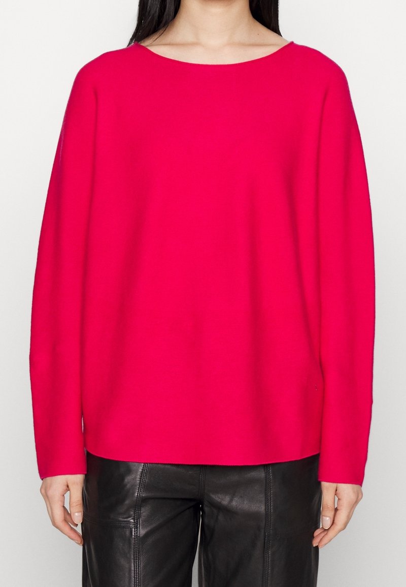 Pull en maille ample de couleur rose vif avec un large décolleté et des manches longues, associé à un pantalon en cuir noir taille haute.