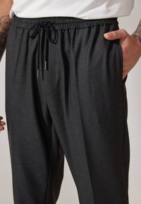 Pantalones jogger gris oscuro con cintura elástica, cordón ajustable y bolsillos laterales. Textura suave y corte ajustado.