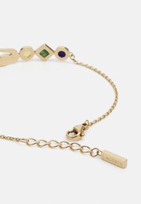 Gouden kettingarmband met kleurrijke geometrische accenten: geel, groen en blauw. Inclusief een sluiting en gegraveerd Lacoste-label.