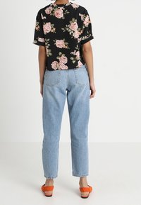 Top nero a maniche corte con fantasia floreale; jeans high-waisted azzurri; sandali arancioni; vista posteriore che mostra il motivo a rose e vestibilità rilassata.