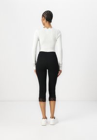 Haut à manches longues blanc à côtes avec des accents en dentelle aux poignets, associé à un legging noir coupé avec une finition en dentelle à l'ourlet, porté avec des baskets blanches.