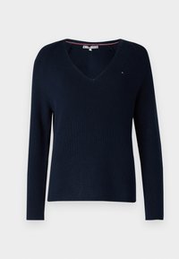 Pull en maille bleu marine à manches longues avec col en V et petit logo brodé sur la poitrine, présenté sur un fond uni.