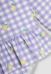 Paarse gingham-gepatroneerde stof met gele citroenenprints. Heeft een gerimpelde zoom en lange mouwen, gemaakt van een soepele stof.