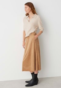 Golfino a maglia beige con maniche corte, abbinato a una gonna plissettata color sabbia lunga fino alla caviglia e stivali con zeppa neri.