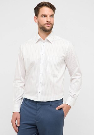 Witte blouse met lange mouwen met lichte verticale strepen, voorzien van een borstzak en een kraag met knoopsluiting. De stof lijkt glad en licht van gewicht.