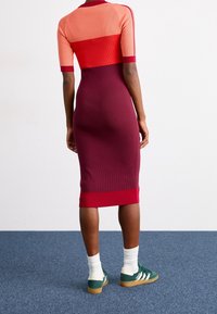 Figurvänlig klänning med ribbad textur, med färgblock i orange, röd och vinröd. Kombinerad med gröna sneakers och vita strumpor.