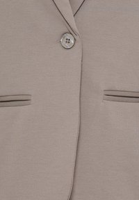 Blazer beige avec un bouton fermé et deux poches à fente horizontale à l'avant.