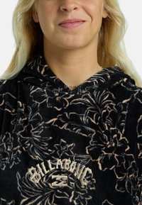Sudadera de felpa negra con estampado floral en tonos claros, que presenta un logo en la parte frontal en color beige. Capucha con cordones y textura suave.