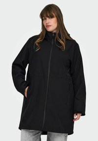 Chaqueta impermeable negra con un collar alto, cremallera completa, mangas largas y bolsillos laterales. Textura suave y un diseño de corte recto.