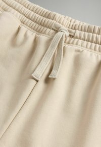 Beige joggers met een elastische tailleband en een trekkoord. De stof heeft een zachte textuur en een gladde afwerking.