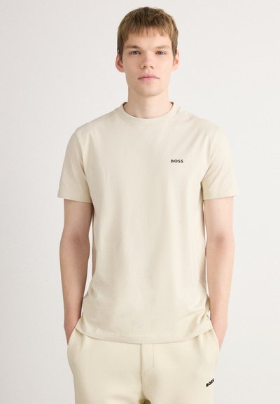 T-shirt beige à manches courtes en tissu lisse, dotée d'un col rond et d'un petit logo "BOSS" noir sur la poitrine gauche.