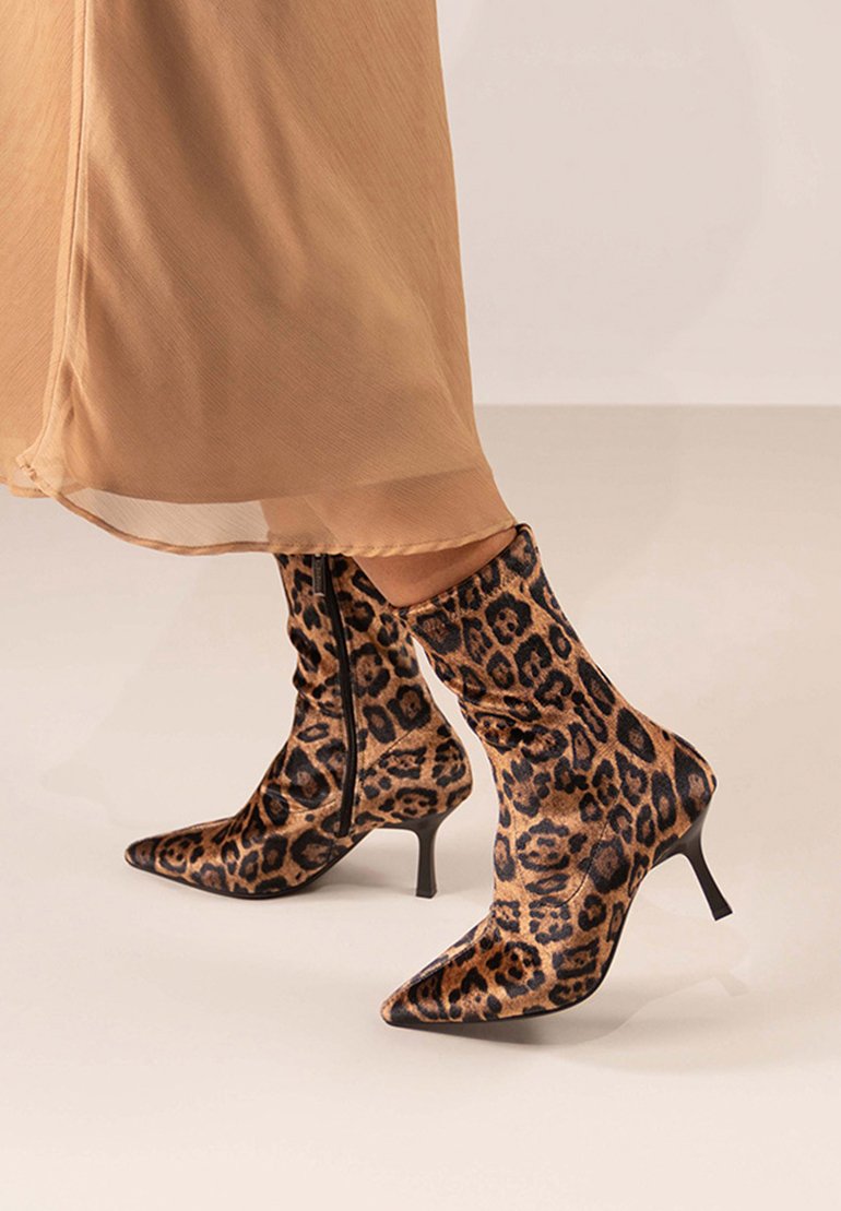 Botas de tobillo de estampado de leopardo con un ajuste ceñido, punta afilada, tacón alto negro y detalle de cremallera lateral, fabricadas con un tejido suave y texturizado.