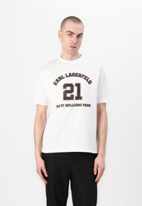 Hvit bomull T-skjorte med svart og gull trykt tekst. Har "KARL LAGERFELD," "21," og "RUE ST-GUILLAUME PARIS" i fet typografi.