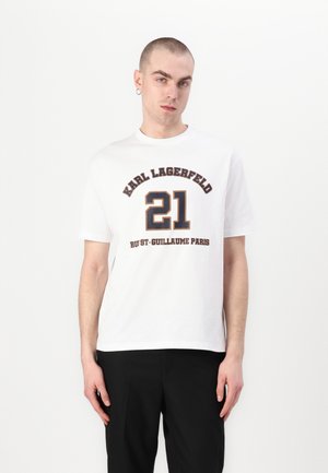 White cotton t-shirt with black and gold printed text. Features "KARL LAGERFELD," "21," and "RUE ST-GUILLAUME PARIS" in bold typography.