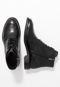 Botas de cuero negras hasta el tobillo con diseño de punta de ala, cierre de cordones y cremallera. Presenta acentos texturizados y un tacón bajo y resistente.