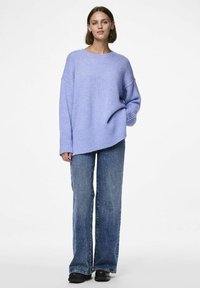 Lichtpaarse gebreide sweater met een losse pasvorm en ribbelrand, gecombineerd met donkerblauwe flared jeans en zwarte platform schoenen.