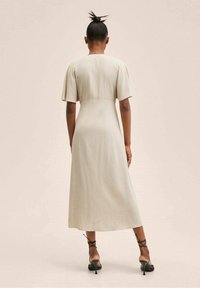 Robe beige longueur genou avec manches courtes, corsage ajusté et jupe fluide. Tissu texturé avec une finition lisse. Talons noirs à lanières.