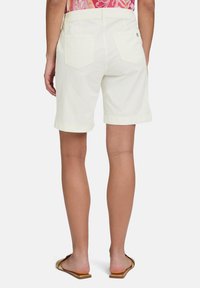 Białe bawełniane szorty o prostym kroju, z dwiema tylnymi kieszeniami i podwiniętymi mankietami, zestawione z płaskimi sandałami w kolorze złotym.