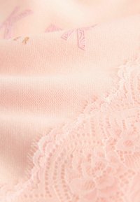 Tissu rose clair présentant une texture lisse avec des détails en dentelle florale en relief sur un bord, complété par des lettres dorées subtiles.