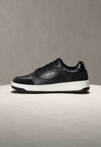 Črni usnjeni nizki supergi z belo podplatom, z blagovno znamko "Just Cavalli" na strani in peti, prikazani na svetli površini z nevtralnim ozadjem.