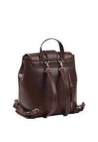 Brun läderryggsäck med dubbla handtag i toppen, justerbara axelremmar och en sidogylf. Har detaljer i guld.