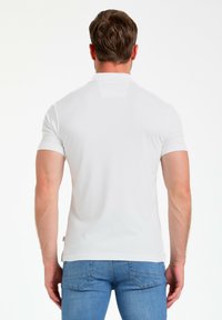 Camisa polo blanca de manga corta con cuello, textura suave y dobladillo recto, combinada con jeans de denim azul claro.