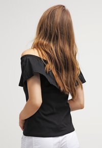 Svart off-shoulder topp med volangärmar, slätt tyg, figurnära design och en ren, enkel bakvy. Inga synliga mönster eller accenter.