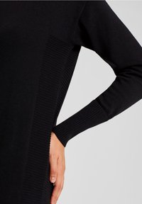 Pull en tricot noir avec une texture côtelée sur les côtés et les manches, au design ajusté et aux manches longues.