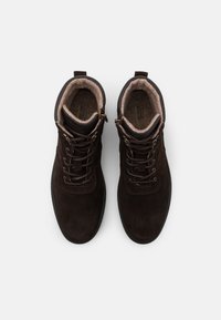 Brown suede boots with a padded interior, lace-up design, and metal eyelets. Features a looped heel for easier wear. Flat rubber sole.