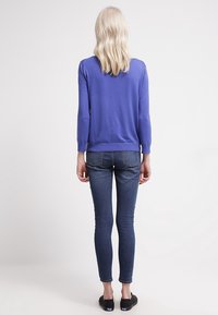 Fioletowy sweter dzianinowy z okrągłym dekoltem, rękawami o długości trzech czwarte, i prążkowanym wykończeniem, zestawiony z ciemnoniebieskimi dopasowanymi dżinsami i czarnymi butami.