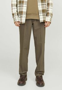 Brun rutigt flanellskjorta över en olivgrön sweatshirt, tillsammans med bruna raka byxor och mörkbruna skor.