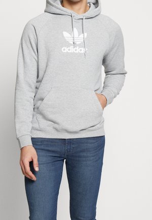 Felpa grigia con tasca a marsupio, logo Adidas bianco, maniche raglan e cappuccio con cordino. Tessuto morbido, vestibilità casual e polsini a coste.