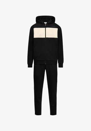 Tuta nera con striscia orizzontale color crema sul petto, felpa con cappuccio e zip con coulisse, e pantaloni coordinati.