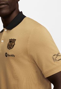 Beige polo-shirt med sort krave, med broderet klublogo og Spotify-branding. Tekstureret stof og standard pasform.