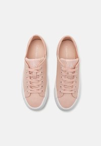 Light pink canvas sneakers with white rubber soles, featuring rounded toe, laces, and subtle branding on the tongue. Flat design and textured upper.