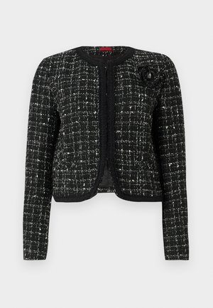 Black and white tweed jacket with a textured finish, structured fit, round neckline, and floral accent on the left shoulder.