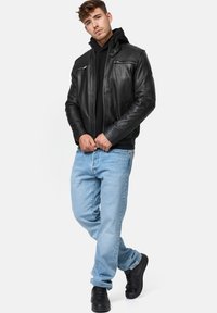 Jachetă neagră din piele, cu buzunare cu fermoar, purtată peste un hanorac negru, asociată cu blugi deschiși la culoare și adidași negri. Outfit urban casual.