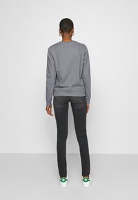 Sudadera de algodón gris con cuello redondo, combinada con jeans de mezclilla oscuros y zapatillas blancas con acentos verdes.